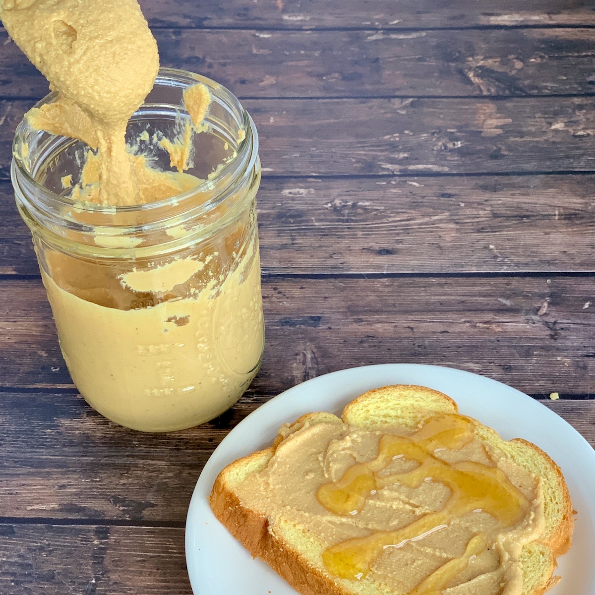 open face peanut butter & honey sandwich with spoon pouring into jar