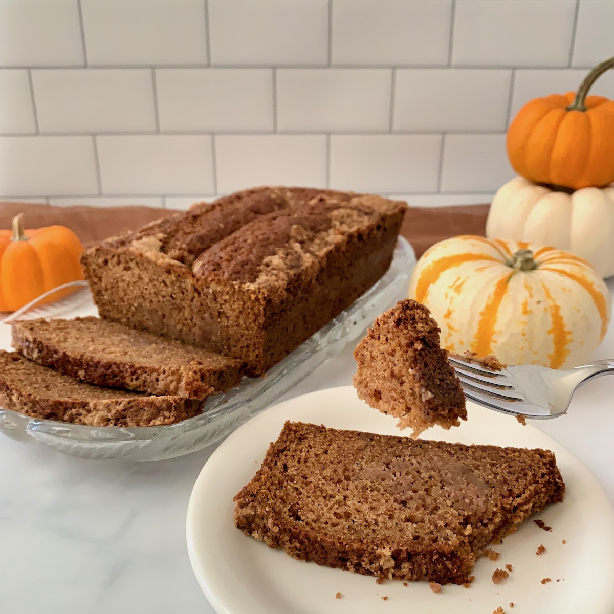 Sourdough Spice Cake slice on plate with bite on fork and loaf behind pumpkins