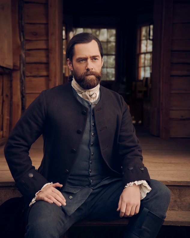 Roger MacKenzie seated on the steps of the Big House in a season 6 promotional still