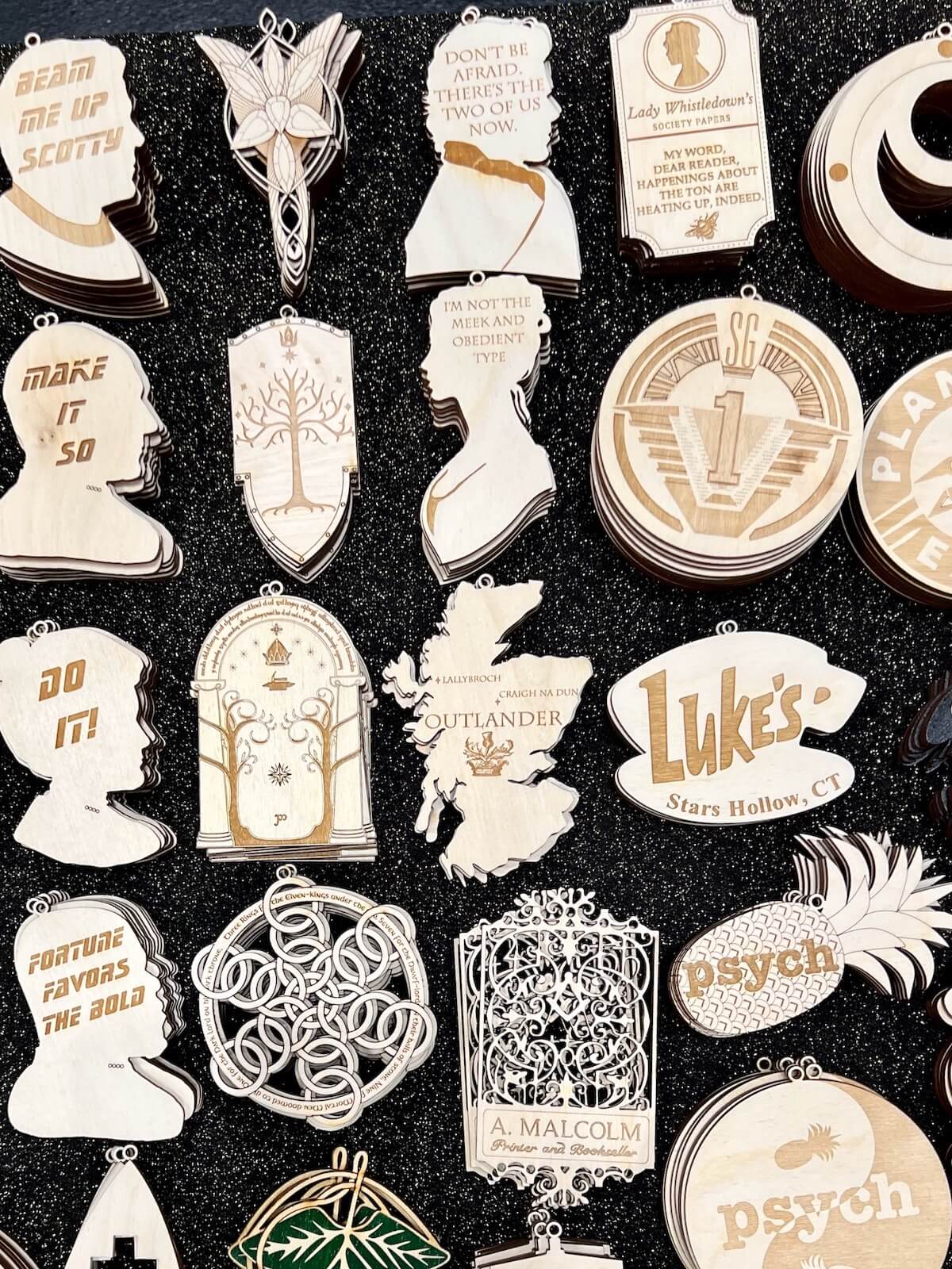 A display full of laser cut wooden ornaments from different fandoms, including Outlander.o