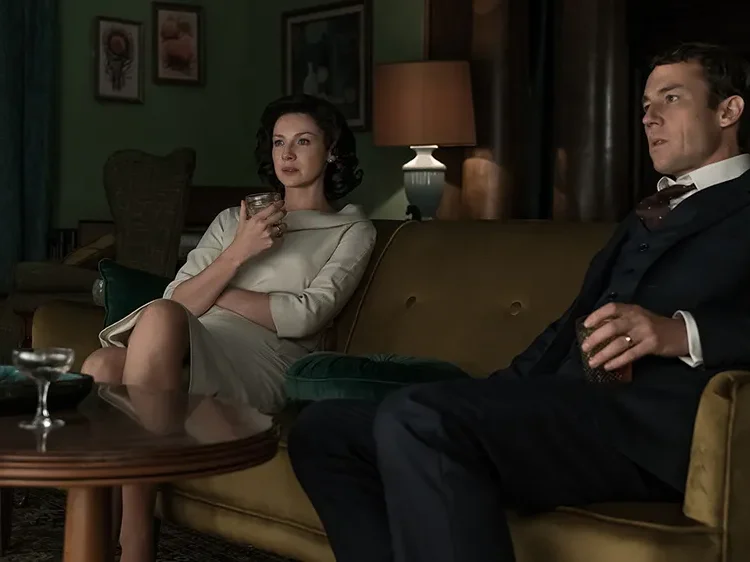 Full spoilers for Outlander Season 3 Episode 3, “All Debts Paid.” This podcast page is spoiler-free for future book events beyond this episode. In this episode of Outlander Cast, Mary recaps and reacts to Outlander Season 3 Episode 3, “All Debts Paid,” live from Martha’s Vineyard with members of the Outlander Cast staff. Blake joins from afar, emotionally unwell about saying goodbye to Frank Randall, and returns at the end to promise many more Frank feelings in the listener feedback episode. Quick answer: “All Debts Paid” is the episode where Frank Randall’s goodbye hurts more than it probably should. Frank dies after years of trying, failing, loving Brianna, resenting Claire, and living inside a marriage that never fully survived Jamie. At the same time, Jamie meets Lord John Grey at Ardsmuir, Murtagh returns, and Season 3 opens a new emotional lane for Jamie after years of grief, prison, and survival. That is what makes the episode so specific. It is not simply “the episode where Frank dies” or “the episode where Lord John shows up.” It is the episode where Outlander asks us to feel the weight of a man many viewers were ready to lose — and then complicates that feeling by reminding us that Frank was Claire’s first love, Brianna’s father in every meaningful daily sense, and one half of a marriage that was never clean enough to hate. Start With Our Outlander Season 3 Guide This episode continues the Voyager arc, moves Jamie deeper into Ardsmuir, and closes a major chapter in Claire’s twentieth-century life. For every Season 3 podcast, recap, listener feedback episode, article, and explainer, start with our Outlander Season 3 Episode Guide. Listen And Watch: Outlander Season 3 Episode 3 Recap & Reaction Watch our full Outlander Season 3 Episode 3 recap and reaction for “All Debts Paid” below. This episode of Outlander Cast covers Frank’s death, Tobias Menzies’ farewell, Claire’s complicated goodbye, Lord John Grey’s introduction, Jamie’s role as leader at Ardsmuir, Murtagh’s survival, David Berry’s casting, the show’s adaptation choices, and why Season 3 feels like the show is back on track. More Coverage For All Debts Paid Want to keep going with this episode? These are the most directly related Outlander Cast pieces from our archive. Minute-By-Minute Recap: Outlander Season 3 Episode 3: the full beat-by-beat breakdown of “All Debts Paid.” All Debts Paid Listener Feedback / Mary & Blake’s Take: Blake returns with his full thoughts on Frank, Claire, Jamie, Lord John, and Murtagh. STARZ Casts Lord John Grey: our original coverage of David Berry joining Outlander. Oh, Frank: our complicated journey of feelings about Frank Randall. Outlander Season 3 Episode 3 Recap: What Happens In All Debts Paid? “All Debts Paid” splits its time between Claire and Frank’s final years in Boston and Jamie’s imprisonment at Ardsmuir. In Boston, Claire continues medical school, Brianna grows older, and the emotional distance between Claire and Frank becomes impossible to pretend away. Their marriage has become an arrangement built around Brianna, history, grief, duty, resentment, and the memory of a man Frank can never fully compete with. Frank eventually asks Claire for a divorce and tells her he plans to move to England with Sandy. The fight that follows is ugly, honest, and long overdue. Frank wants a life where he is not living in Jamie Fraser’s shadow. Claire wants to keep Brianna. Neither of them can pretend this marriage is working, but neither of them gets the mercy of a clean goodbye. In the eighteenth century, Jamie is at Ardsmuir Prison, where he has become the unofficial leader of the Scottish prisoners. Lord John Grey arrives as the new governor, young and eager to prove himself, and immediately finds himself drawn into Jamie’s gravity. Their dinners, chess games, conversations, and shared grief over Culloden begin a complicated relationship built from power, respect, attraction, loneliness, and danger. Why Frank’s Goodbye Hurts More Than It Should Frank Randall should be easy to lose by this point. He is not Jamie. He is not Claire’s great love. He has been angry, wounded, controlling, proud, lonely, and at times brutally unfair. The show has also spent years asking us to sit with his pain, his patience, his decency, his jealousy, and the impossible position he accepted when Claire returned pregnant with another man’s child. That is why his goodbye hurts more than it should. Frank is not the romantic answer to Claire’s life, but he is not nothing. He gave Brianna a father. He gave Claire a home when she had nowhere else to go. He tried to build a marriage on top of a ghost and eventually became bitter because ghosts do not leave room in the bed. The episode works because it refuses to let us flatten him. Frank can be wrong and still be mourned. Claire can love Jamie and still grieve Frank. Brianna can be Jamie’s daughter by blood and Frank’s daughter by life. “All Debts Paid” understands that emotional debt is not paid just because someone dies. Tobias Menzies Gets The Farewell Frank Deserves This episode is also a farewell to Tobias Menzies, and that matters because he carried two of the show’s most difficult roles. As Black Jack Randall, he embodied horror, control, cruelty, and violation. As Frank, he played restraint, hurt, intelligence, repression, and the slow rot of a man trying to survive a marriage he knows he cannot fully have. The brilliance of Tobias Menzies is that he never made Frank a saint simply because Black Jack was a monster. Frank has edges. Frank has resentment. Frank has flashes of anger that remind the audience why Claire’s life with him could never be emotionally simple. At the same time, he also has enough humanity that his death cannot be shrugged off. That is why the morgue scene lands. It is not only Claire saying goodbye to Frank. It is the show saying goodbye to an actor who helped define the first three seasons. Whether we love Frank, hate Frank, defend Frank, or want him to get out of the way, the story is different without him. Claire’s Goodbye Is Complicated Because Frank Was Her First Love Claire telling Frank that he was her first love is important because it gives their relationship history back. It reminds us that Frank was not always the man standing between Claire and Jamie. Before the stones, before Black Jack’s shadow, before Culloden, before Brianna, before the impossible bargain of Boston, Frank was the person Claire chose. That does not mean Frank is her great love. The show is not confused about that. Jamie is the love that reorders Claire’s entire life. But Frank is part of who Claire was before Jamie, and that matters. Her grief in the morgue is not the grief of a woman who wishes she had chosen differently. It is the grief of a woman who knows something real existed once, even if it could not survive what happened later. The line “if you’re still close enough to hear me” gives the scene a soft, almost Highlander feeling. Claire has lived too long with stones, ghosts, time travel, and impossible love to treat death as purely clinical. She is a doctor, but she is also a woman who knows that some presences linger. Frank’s Death Works Because We Do Not See The Crash One of the smartest craft choices in “All Debts Paid” is that we do not need to see Frank’s car accident. The episode could have turned the death into a spectacle. Instead, it makes the emotional aftermath the point. That restraint works because Frank’s death is not about impact, metal, glass, or road conditions. It is about the fact that he leaves after a fight and never comes home. That kind of suddenness is ordinary and horrifying. People say unfinished things. People walk out angry. People assume there will be another conversation. Sometimes there is not. By keeping the crash offscreen, the episode keeps us with Claire. We experience Frank’s death the way she does: as news, as shock, as a body, as a goodbye she did not know she was already saying. Lord John Grey Arrives As A Mirror, Not Just A New Character Lord John Grey’s arrival at Ardsmuir is not simply the introduction of a fan-favorite character. It is the beginning of a relationship that immediately complicates Jamie’s prison life. John is young, polished, ambitious, and trying to perform authority in a place where Jamie already has the men’s loyalty without asking for it. That contrast is what makes the dynamic interesting. John has the title. Jamie has the gravity. John runs the prison. Jamie leads the prisoners. John can invite Jamie to dinner, offer food, play chess, and ask questions, but he cannot command the kind of respect Jamie carries by existing. The episode also gives John enough vulnerability to make him more than a uniform. His grief over Culloden, his brother, and the man he loved opens a door between him and Jamie. For a moment, they are not only jailer and prisoner. They are two men who know what it means to lose someone and keep breathing anyway. Jamie At Ardsmuir Is Still A Leader Without Trying One of the best Jamie choices in “All Debts Paid” is that he does not need to fight for leadership. He simply has it. The other prisoners look to him because he is Red Jamie, because he survived Culloden, because he tried to stand with them, and because he carries himself like a man whose authority does not depend on freedom. That is a major contrast with Claire’s twentieth-century story. Claire has to fight constantly to be taken seriously in medical school, at work, and in her own home. Jamie, even imprisoned, is recognized as a leader almost by default. That does not mean his life is easy. It means the episode is showing two different kinds of power: the power Jamie carries naturally in a male, martial world, and the power Claire has to carve out in a world designed to doubt her. That parallel is one of the reasons Season 3 works. Jamie and Claire are separated by centuries, but their stories keep speaking to each other. He is trapped in a prison and still leads. She is free in Boston and still has to fight for room. Murtagh Lives, And The Show Changes The Emotional Math The reveal that Murtagh survived is one of the episode’s biggest emotional jolts. For viewers who love him, it is a relief. For book readers, it is a major adaptation choice. Either way, the moment changes the emotional math of Jamie’s prison life. Jamie is still lonely. He is still separated from Claire. He is still imprisoned. But Murtagh’s presence means Jamie is not completely alone inside Ardsmuir. That matters because Murtagh is not just a familiar face. He is family, witness, history, and a living connection to the life Jamie lost. The challenge is that the show now has to make that choice matter. Keeping Murtagh alive cannot only be a crowd-pleasing reveal. It has to create story. It has to change Jamie’s emotional reality. In this episode, at least, it does. Seeing Murtagh again gives the prison story warmth, continuity, and a little bit of hope. The Adaptation Debate: Does The Show Make Frank Too Sympathetic? One of the biggest conversations around “All Debts Paid” is whether the show’s version of Frank changes too much from the books. The open marriage detail, the way blame lands on Claire, and the way Frank is framed as wounded and sympathetic all push the audience toward a more complicated view of him. That choice works better if we judge show Frank as show Frank. The television version has been built consistently as a man who is decent, flawed, jealous, wounded, and trying to live with something almost no one could live with cleanly. That does not mean he is always right. It means the show has chosen to make his pain emotionally legible. The risk is that Claire can look colder by comparison. If Frank is constantly framed as the man trying and Claire is framed as the woman withholding, the story can feel like it is drifting away from Claire’s interior life. That is the tension this episode sits inside. It gives Frank a powerful farewell, but it also has to make sure Claire remains the center of her own story. Bear McCreary’s Frank Theme Does The Emotional Work Frank’s farewell also works because of the music. The clarinet line in Frank’s theme carries a very specific kind of ache. It is not triumphant, romantic, or melodramatic. It feels like memory. It feels like something that once mattered and can no longer be recovered. That is exactly what the episode needs. Frank and Claire’s marriage is not something the audience is meant to cheer for in the same way we cheer for Jamie and Claire. But the music reminds us that this was still a life. There was a first love here. There was a second honeymoon. There were real smiles before everything became haunted. The score gives Frank dignity without pretending he was the answer. That is a delicate balance, and the episode needs it. Why All Debts Paid Makes Season 3 Feel Like Outlander Is Back Part of the excitement around this episode is that Season 3 feels like Outlander is back on track. The Scotland material has texture again. Ardsmuir gives Jamie a new social world. Claire’s Boston life is emotionally fraught but thematically connected. Lord John brings a new kind of tension. Frank’s death closes one story while forcing us to feel the cost of its ending. The episode also makes the season feel bigger without becoming scattered. Boston, Ardsmuir, Brianna, Frank, Joe, Murtagh, Lord John, and Jamie could easily feel like too much. Instead, they orbit the same question: what do people become after the life they wanted is gone? Frank becomes a man trying to start over too late. Claire becomes a doctor and a widow. Jamie becomes a prisoner who still leads. Lord John becomes a young officer already pulled toward the most dangerous person in the room. Murtagh becomes proof that the past is not finished speaking. Mary & The Outlander Cast Staff’s Kilt Ratings For All Debts Paid The live Martha’s Vineyard panel gave “All Debts Paid” strong ratings, with several people landing around five kilts and others leaving just a little room for the season to climb even higher. The shared feeling was clear: Season 3 has momentum, and this episode keeps the show in the emotional and visual lane that made people fall in love with Outlander in the first place. The highs were Frank’s theme, Claire’s costumes, Joe Abernathy, Murtagh’s return, Lord John’s arrival, Jamie’s face when he talks about Claire, the Scotland visuals, and the sense that the show is finally letting the parallel lives structure do real work. The complaints were also specific: Frank’s glasses, Sandy showing up at the worst possible moment, the open marriage adaptation choice, and the compressed speed of the Ardsmuir relationship. That balance is what makes the episode worth talking about. It is emotional, effective, and important, but not without choices worth debating. That is the sweet spot for a great Outlander Cast episode. Outlander Season 3 Episode 3: The Craft Verdict “All Debts Paid” works because it understands that closure should not feel clean. Frank’s death does not fix Claire’s grief. It does not erase resentment. It does not magically make Jamie closer. It simply ends a chapter that was already ending and leaves Claire to feel the weight of what was real, what was broken, and what can never be repaired. The Ardsmuir material works for the opposite reason. It opens something instead of closing it. Jamie and Lord John’s relationship begins with authority and curiosity, then quickly gathers grief, attraction, discomfort, respect, and danger. Murtagh’s survival adds warmth and risk. Jamie’s leadership gives the prison story a center. That is why the episode matters. Frank’s goodbye hurts more than it should because the show has done enough work to make him human. Lord John’s arrival matters because the show gives Jamie a new emotional complication before he can ever get back to Claire. “All Debts Paid” is not about settling the past. It is about proving that every paid debt leaves another mark somewhere else. Related Outlander Coverage Outlander Season 3 Episode Guide: every Season 3 podcast, recap, listener feedback episode, and explainer. Minute-By-Minute Recap: All Debts Paid: the full beat-by-beat breakdown of Episode 3.03. All Debts Paid Listener Feedback / Mary & Blake’s Take: more reaction to Frank, Claire, Jamie, Lord John, and Murtagh. Oh, Frank: our complicated journey of feelings about Frank Randall. STARZ Casts Lord John Grey: our original coverage of David Berry joining Outlander. Lord John Grey Cast? early thoughts on one of Season 3’s most important additions. Outlander’s Murtagh Lives: why the show’s major Murtagh change matters. Outlander Timeline Explained: Claire, Jamie, Culloden, the 20-year separation, and the split across centuries. Outlander Season 2 Episode Guide: Faith, Frank, Black Jack Randall, Culloden, and the road into Season 3. Outlander Cast Podcast Hub: browse all of our Outlander recaps, reactions, interviews, and listener feedback episodes. Go Deeper With Mary & Blake Love the craft, character, and emotional analysis behind Outlander? We go deeper on the show in Outlander Cast and inside The Nerd Clan, where members get bonus episodes, Blake’s Book Club, extra analysis, community discussion, and more. Outlander Season 3 Episode 3 recap